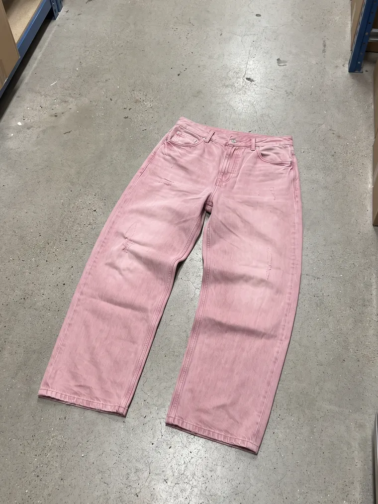 Phone photo: pink jeans flat on a concrete warehouse floor, front